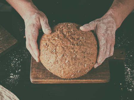 male hands are holding brown baked rye bread , top view, vintage toningの写真素材