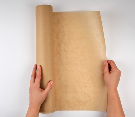 roll of brown parchment paper in female hands, white background, top view