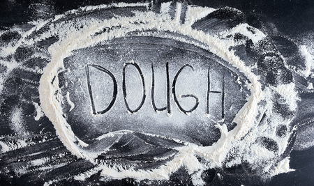 white wheat flour scattered on a black background, product is spread over the surface, kitchen background, inscription doughの写真素材