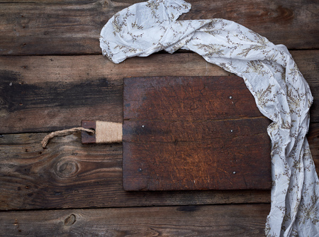 very old empty brown wooden cutting board with handle and kitchen napkin, top view