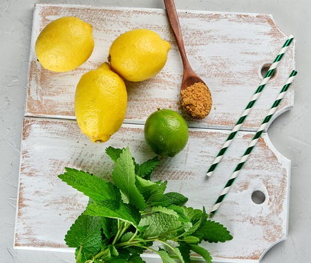 ripe yellow whole lemons and lime, brown sugar and a bunch of fresh mint on a white wooden board, top view, ingredients for lemonadeの写真素材