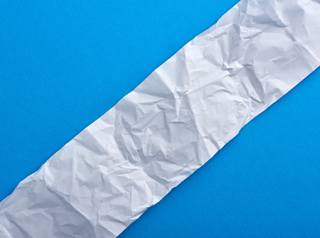 Strip of crumpled blank white paper on a blue background, piece lies diagonally
