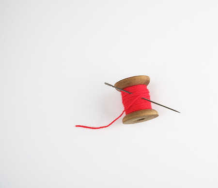 Wooden reel with red wool thread and a large needle, white background, copy space