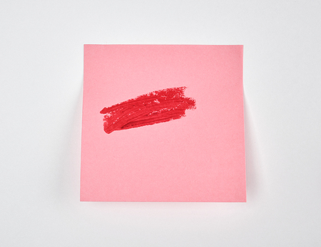 smears of red lipstick on a pink paper sticker, white background