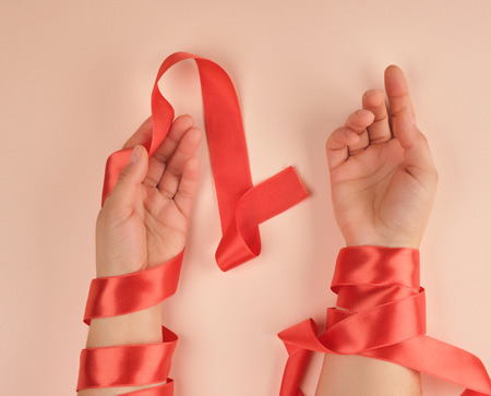 two female hands wrapped in a red satin ribbon, peach background, top viewの写真素材