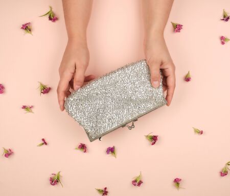 women's hands hold a silver clutch, peach background with blooming buds of pink flower s, top viewの写真素材