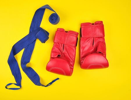 pair of red leather boxing gloves and blue textile bandage on a yellow background, flat lay