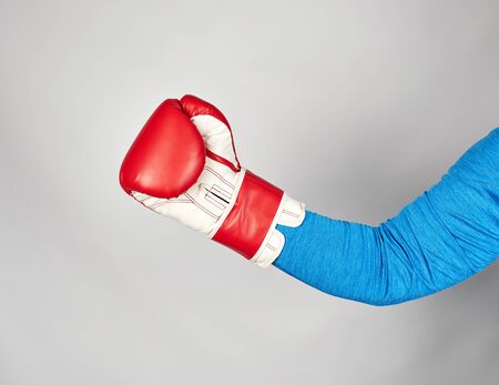 man's hand is wearing a red leather boxing glove on a gray background, sports backdropの写真素材