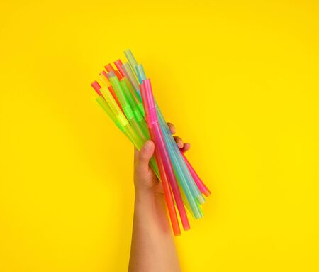 female hand holding multicolored plastic cocktail tubes, yellow backgroundの写真素材