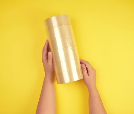 two female hands holding a stack of transparent scotch on a yellow background, adhesive tapeの写真素材