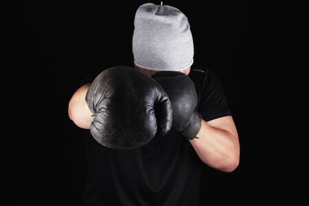 young man stands in a boxing rack, wearing very old vintage brown boxing gloves on his hands, black backgroundの写真素材