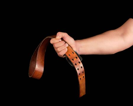 brown leather belt with an iron buckle in a man's hand, black backgroundの写真素材