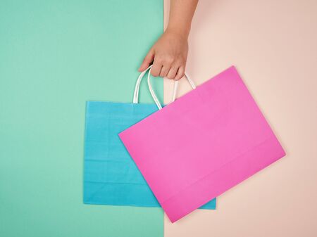 hand holding two paper shopping bags on a pastel background, concept of seasonal salesの写真素材