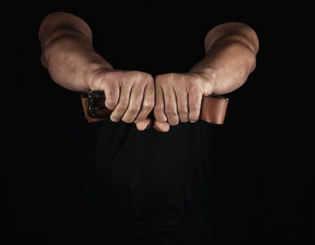 adult man in black clothes holding a brown leather belt with an iron buckle, concept of violence and...