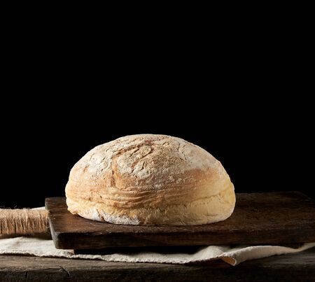 baked round white wheat bread on a textile towel, wooden old table, black background. Homemade food