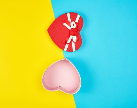 open red heart-shaped gift box with a bow on a blue yellow background, top view, festive backdrop