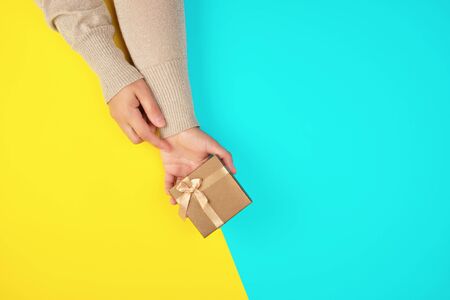 two hands hold a paper closed golden box on a yellow blue background, festive backdropの写真素材