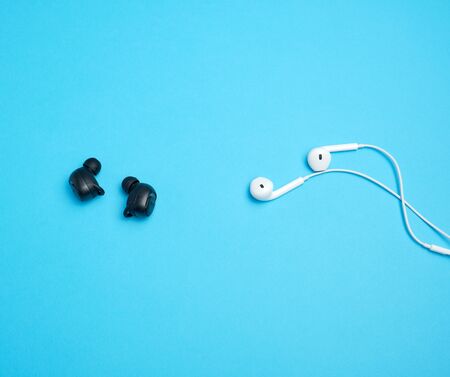 black wireless and white earphones with wire on a blue background, technology conceptの写真素材