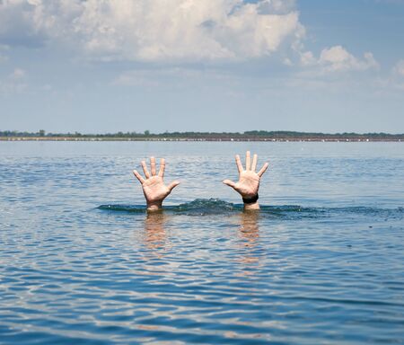 pair of masculine hands sticks out of the sea water on a summer day, gesture of a man who sinks