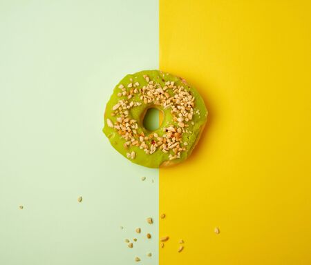 round sweet green pistachio donut sprinkled with ground nut on a yellow background, top viewの写真素材