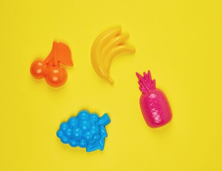 multicolored plastic toys fruits on a yellow  background, copy spaceの写真素材