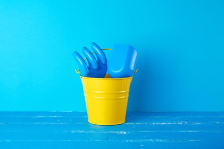 yellow children's metal bucket and plastic shovel and rake on a blue background, concept of sea holidaysの写真素材