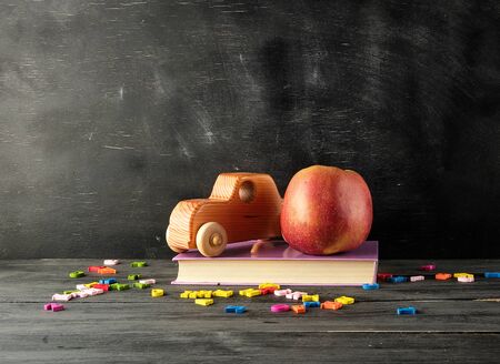ripe red apple, ancient toy car stand on a book, background from an empty black chalk boardの写真素材
