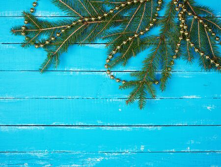 green branches of needles and yellow Christmas garland on a blue wooden background from boards, copy spaceの写真素材