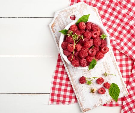 ripe red raspberries in a white wooden plate on a table of boards, textile towel, top viewの写真素材