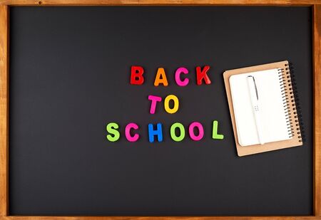 inscription back to school from multi-colored plastic letters and a stack of spiral notebooks on a...