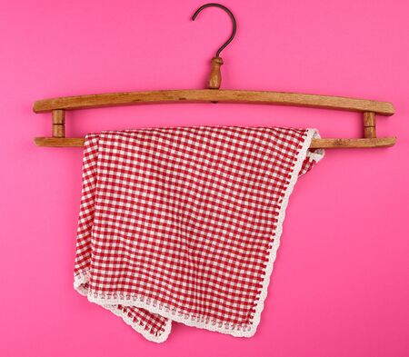 red checkered kitchen towel hanging on a vintage wooden hanger, pink background