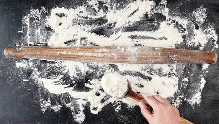 very old brown wooden rolling pin and female hand on a black background with white wheat flour, top viewの写真素材