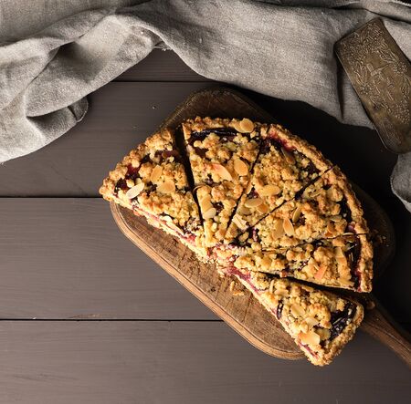 half plum pie crumble on a brown wooden cutting board, top view