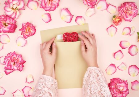 two female hands put a red heart in a brown paper envelope, concept of congratulations on the holiday and loveの写真素材