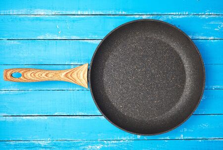 new empty frying pan with a brown handle on a blue wooden background, bottom with a crumb of stone and marbleの写真素材