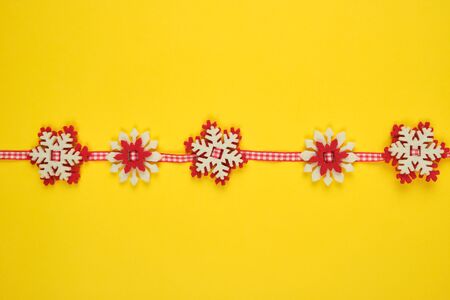 Christmas garland with carved felt snowflakes on a red ribbon, yellow backgroundの写真素材