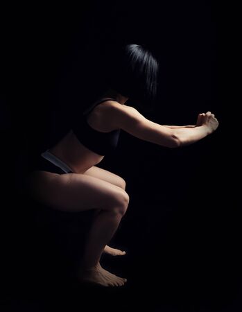 beautiful young girl of athletic appearance with black hair does squats, low keyの写真素材