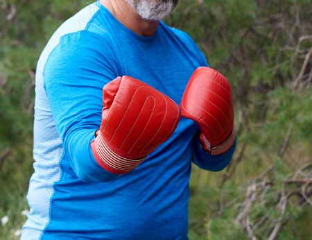 adult plump athlete in blue uniform and red leather boxing gloves stand in the middle of a green meadow, concept of doing sports in natureの写真素材