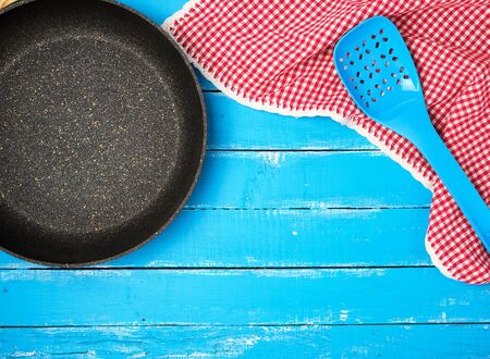 empty black round nonstick frying pan with handle on blue wooden background with red napkin, top viewの写真素材