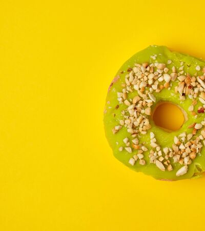 round sweet green pistachio donut sprinkled with ground nut on a yellow background, top viewの写真素材