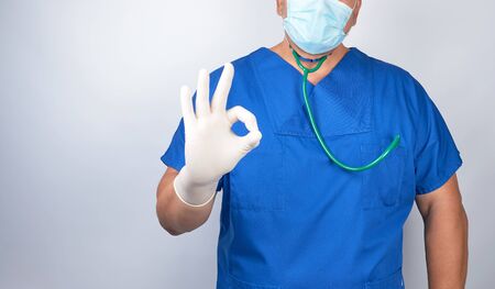 doctor in blue uniform and latex sterile gloves shows an approval symbol with her hand, white background, copy spaceの写真素材