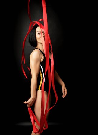 young woman gymnast of Caucasian appearance with black hair spins red satin ribbons, gymnastic exercises on black backgroundの写真素材