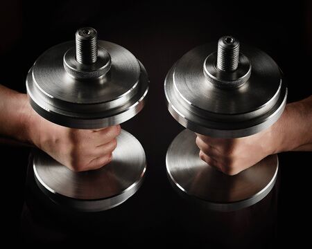 two steel typesetting dumbbells in male hands, sports backdrop, low keyの写真素材