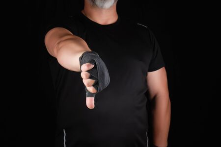 adult athlete in black uniform and hands rewound with textile bandage shows gesture dislike, low keyの写真素材