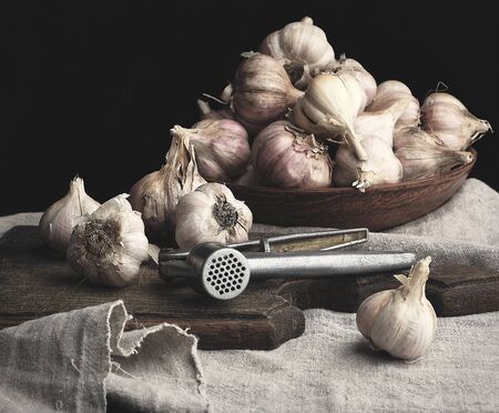 raw unpeeled garlic on a very old vintage cutting board and iron press, dark backgroundの写真素材