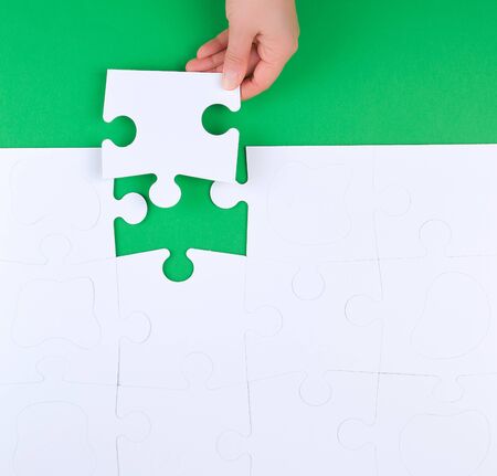female hand puts empty white big puzzles on a green background, top viewの写真素材