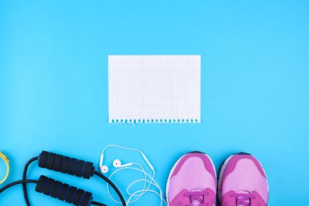 empty white sheet of paper, pink sports sneakers and jump rope on a blue background,  set for schedules and recording workouts, top viewの写真素材