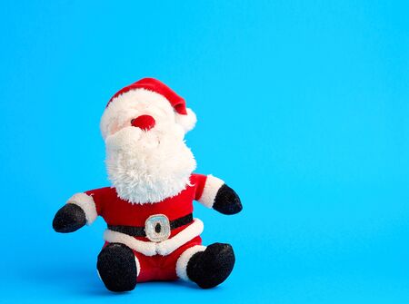 traditional toy santa claus in a red suit and white beard sits on a blue background, copy spaceの写真素材