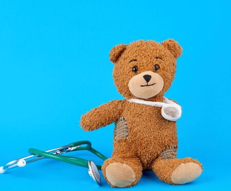 brown teddy bear with a bandaged paw sitting on a blue background, peditry conceptの写真素材