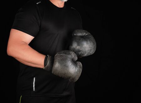 man stands in a boxing rack, wearing very old vintage black boxing gloves on his hands, dark...